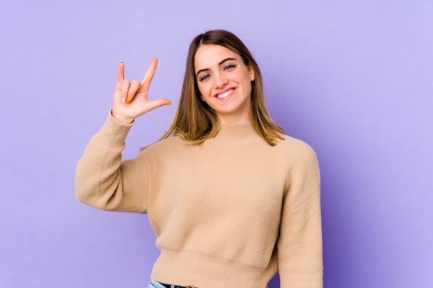 Joven mujer caucásica aislada sobre púrpura mostrando un gesto de cuernos como covercept revolucionario.