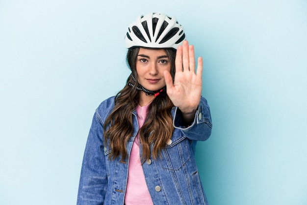 Joven mujer caucásica andar en bicicleta aislado sobre fondo azul de pie con la mano extendida mostrando la señal de stop, impidiéndote.