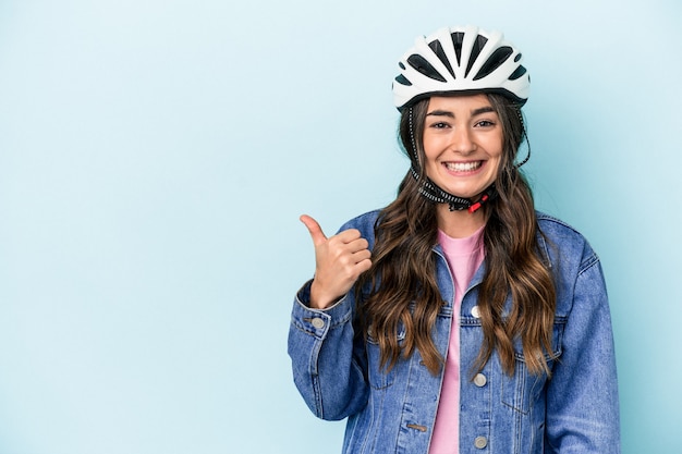 Joven mujer caucásica andar en bicicleta aislado sobre fondo azul sonriendo y levantando el pulgar hacia arriba