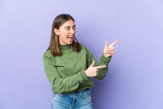 Joven mujer caucásica apuntando con los dedos índices a un espacio de copia, expresando entusiasmo y deseo.