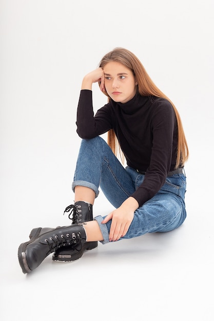 Joven mujer caucásica atractiva en cuello alto negro, jeans azul en estudio blanco