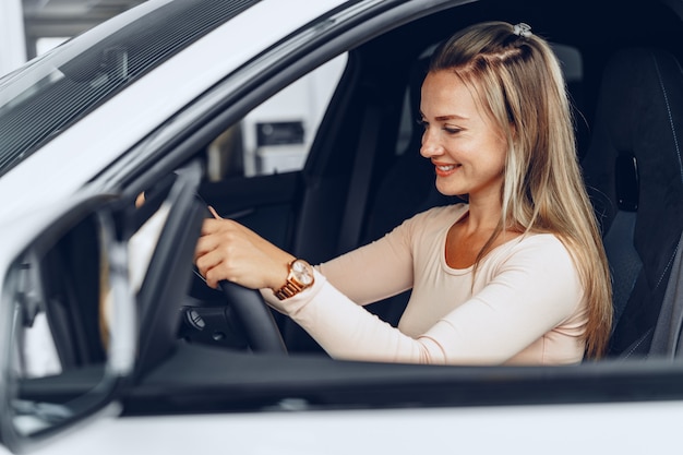 Joven mujer caucásica atractiva se sienta en su coche recién comprado en concesionario