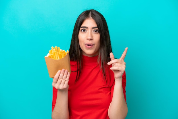 Joven mujer caucásica atrapando papas fritas aisladas de fondo azul con la intención de darse cuenta de la solución mientras levanta un dedo