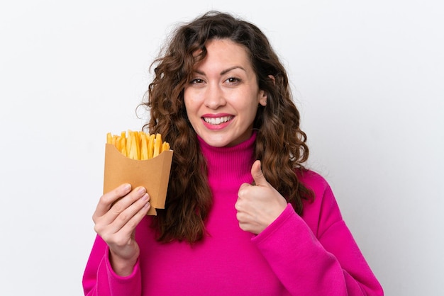 Joven mujer caucásica atrapando papas fritas aisladas de fondo blanco con los pulgares hacia arriba porque algo bueno ha sucedido