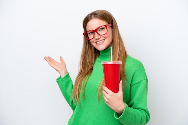 Joven mujer caucásica bebiendo soda aislada de fondo blanco extendiendo las manos a un lado para invitar a venir