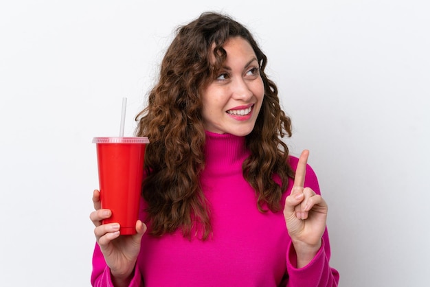 Joven mujer caucásica bebiendo soda aislada de fondo blanco con la intención de darse cuenta de la solución mientras levanta un dedo