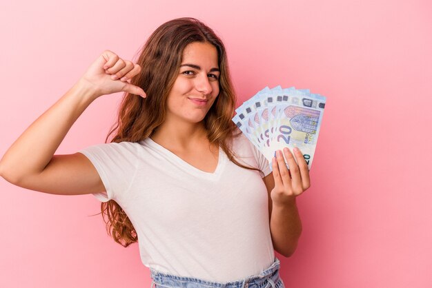 Joven mujer caucásica con billetes aislados sobre fondo rosa se siente orgullosa y segura de sí misma, ejemplo a seguir.