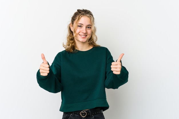 Joven mujer caucásica en blanco sonriendo y levantando el pulgar hacia arriba