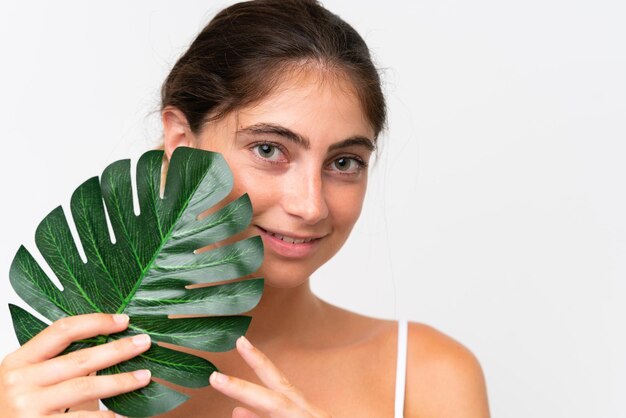 Joven mujer caucásica bonita aislada sobre un fondo blanco sosteniendo una hoja de palma Retrato en primer plano