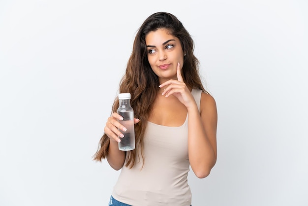 Joven mujer caucásica con una botella de agua aislada sobre fondo blanco pensando en una idea mientras mira hacia arriba