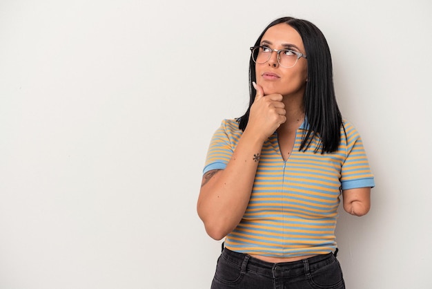 Joven mujer caucásica con un brazo aislado sobre fondo blanco mirando hacia los lados con expresión dudosa y escéptica.