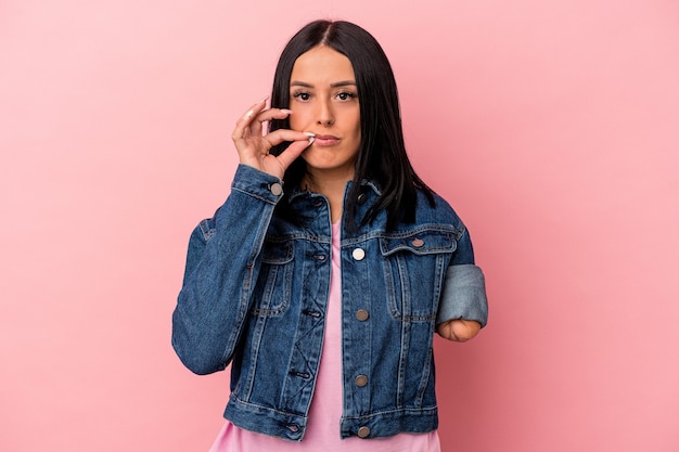 Joven mujer caucásica con un brazo aislado sobre fondo rosa con los dedos en los labios guardando un secreto.