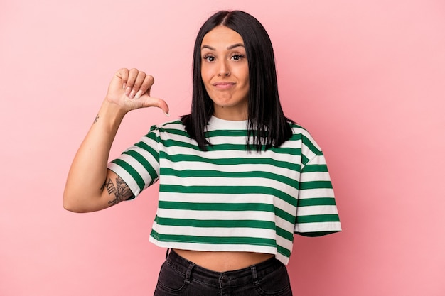 Joven mujer caucásica con un brazo aislado sobre fondo rosa mostrando un gesto de aversión, pulgares hacia abajo. Concepto de desacuerdo.