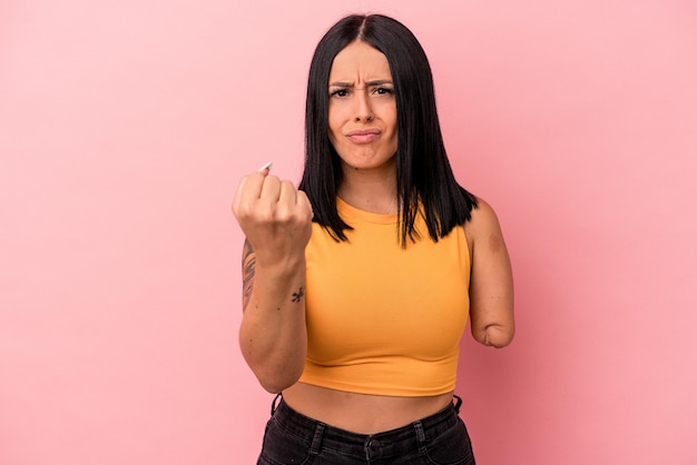 Joven mujer caucásica con un brazo aislado sobre fondo rosa mostrando el puño a la cámara, expresión facial agresiva.