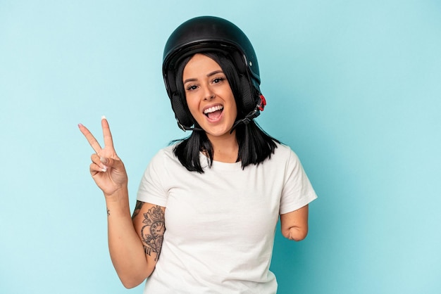 Joven mujer caucásica con un brazo que llevaba un casco de moto aislado o fondo azul alegre y despreocupado mostrando un símbolo de paz con los dedos.