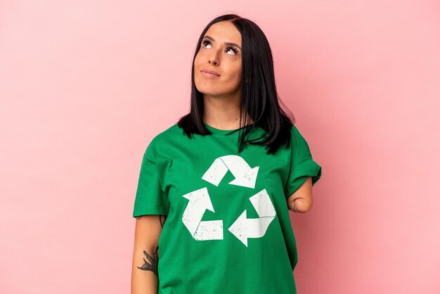 Joven mujer caucásica con un brazo reciclado residuos aislados sobre fondo rosa soñando con lograr metas y propósitos
