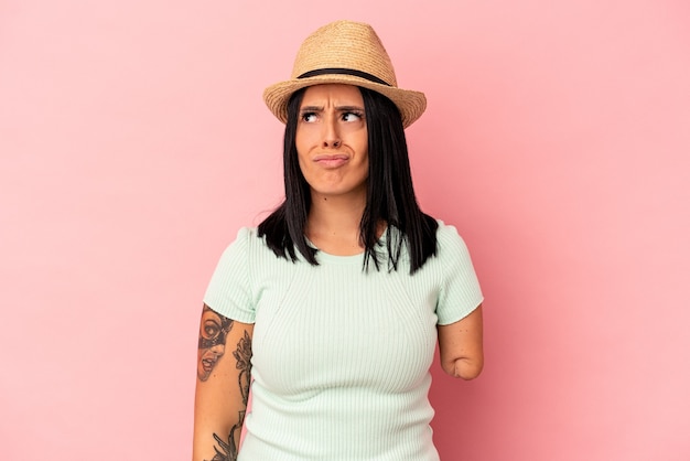 Joven mujer caucásica con un brazo con un sombrero de verano aislado sobre fondo rosa confundida, se siente dudosa e insegura.