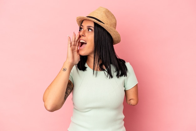 Joven mujer caucásica con un brazo con un sombrero de verano aislado sobre fondo rosa gritando y sosteniendo la palma cerca de la boca abierta.
