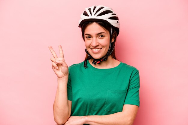 Joven mujer caucásica con casco aislado de fondo rosa que muestra el número dos con los dedos