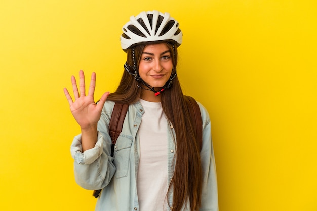 Joven mujer caucásica con un casco de bicicleta aislado en la pared amarilla sonriendo alegre mostrando el número cinco con los dedos.