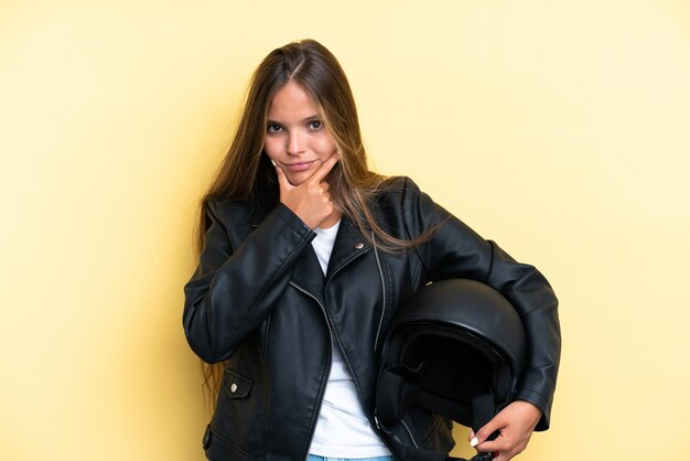 Joven mujer caucásica con un casco de motocicleta aislado sobre fondo amarillo pensando