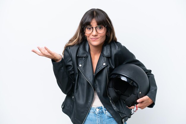 Joven mujer caucásica con un casco de motocicleta aislado sobre fondo blanco con dudas mientras levanta las manos