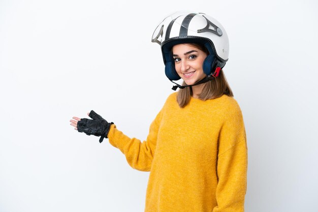 Joven mujer caucásica con un casco de motocicleta aislado sobre fondo blanco extendiendo las manos hacia el lado para invitar a venir