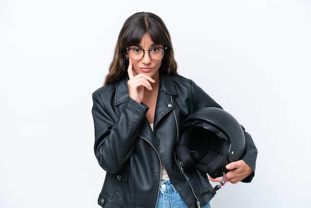 Joven mujer caucásica con un casco de motocicleta aislado sobre fondo blanco pensando