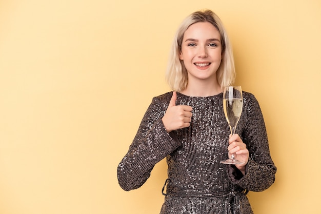 Joven mujer caucásica celebrando el año nuevo aislado sobre fondo amarillo sonriendo y levantando el pulgar hacia arriba