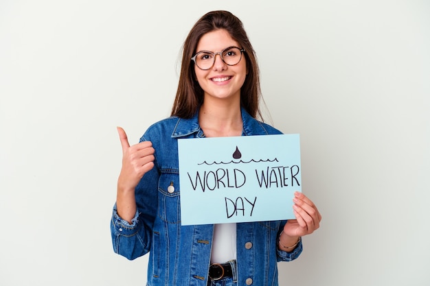 Joven mujer caucásica celebrando el día mundial del agua aislado en rosa sonriendo y levantando el pulgar hacia arriba