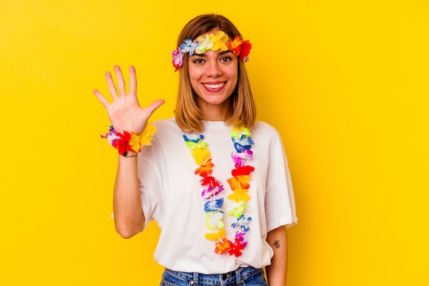 Joven mujer caucásica celebrando una fiesta hawaiana sonriendo alegre mostrando el número cinco con los dedos.