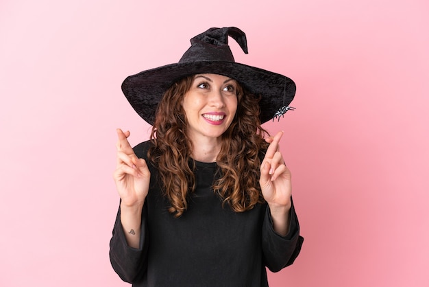 Joven mujer caucásica celebrando halloween aislado sobre fondo rosa con los dedos cruzados