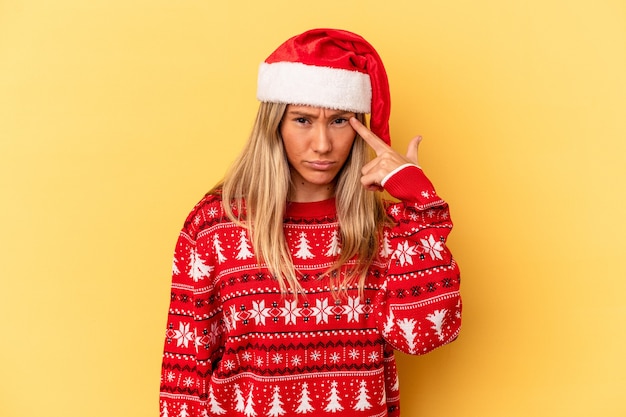 Joven mujer caucásica celebrando la Navidad aislado sobre fondo amarillo mostrando un gesto de decepción con el dedo índice.