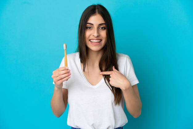 Joven mujer caucásica cepillarse los dientes aislado sobre fondo azul con expresión facial sorpresa