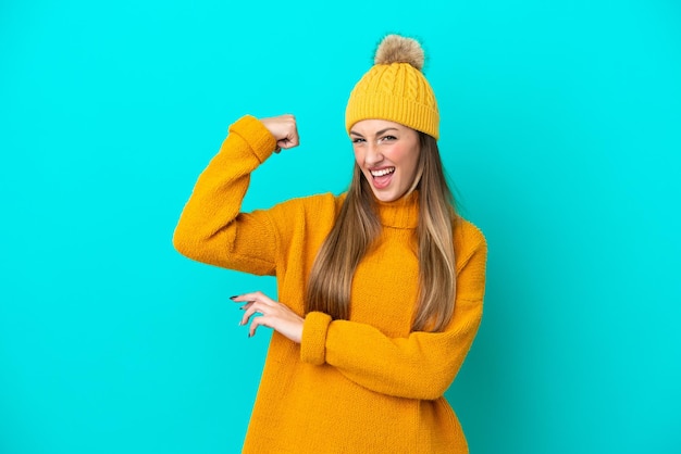 Joven mujer caucásica con chaqueta de invierno aislada de fondo azul haciendo un gesto fuerte