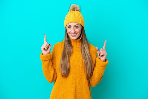 Joven mujer caucásica con chaqueta de invierno aislada de fondo azul señalando una gran idea