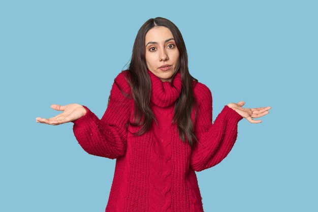 Foto joven mujer caucásica con un cómodo suéter rojo en el fondo del estudio dudando y encogiéndose de hombros