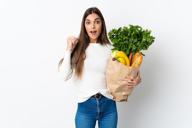 Joven mujer caucásica comprando algo de comida aislado en blanco celebrando una victoria en la posición ganadora