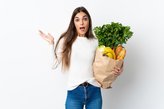 Joven mujer caucásica comprando algo de comida aislado en blanco con expresión facial sorprendida