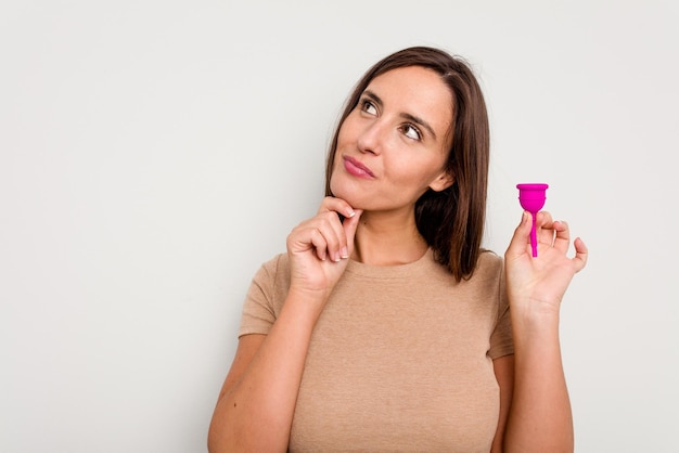 Joven mujer caucásica con copa menstrual mirando hacia los lados con expresión dudosa y escéptica