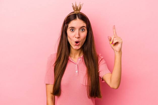 Joven mujer caucásica con corona aislada sobre fondo rosa con una gran idea, concepto de creatividad.