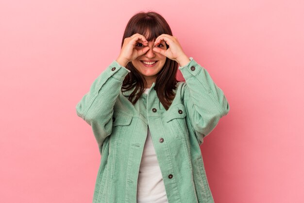 Joven mujer caucásica con curvas aislada sobre fondo rosa mostrando bien firmar sobre los ojos