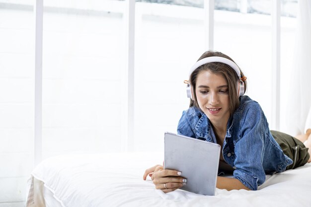 Joven mujer caucásica en disfrutar de la música en línea en la tableta mientras se relaja en la cama con feliz en casa en el dormitorio.