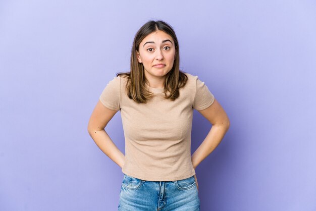 Joven mujer caucásica se encoge de hombros y abre los ojos confundidos.