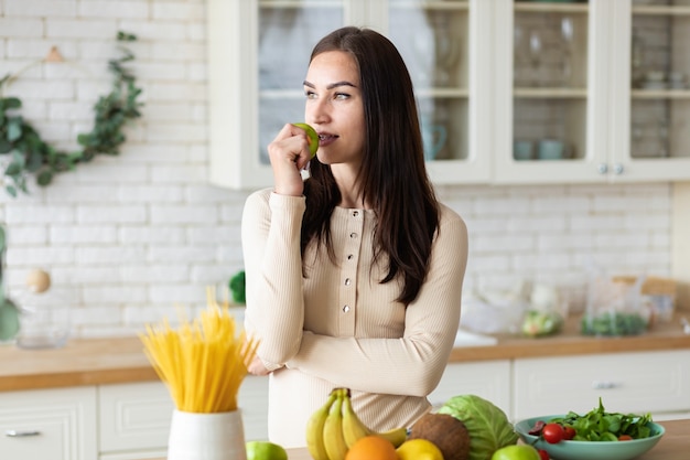 Joven mujer caucásica está de pie en la cocina con una manzana verde en sus manos. Estilo de vida saludable y concepto de comida sana.