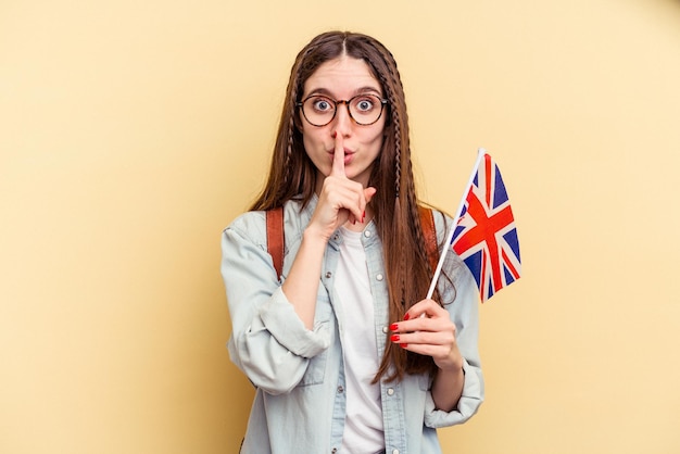 Joven mujer caucásica estudiando inglés aislada de fondo amarillo guardando un secreto o pidiendo silencio