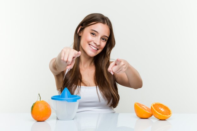 Joven mujer caucásica con un exprimidor de naranjas sonrisas alegres apuntando al frente.