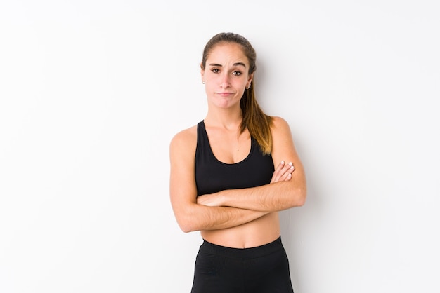 Joven mujer caucásica fitness posando en un espacio en blanco infeliz mirando a puerta cerrada con expresión sarcástica.