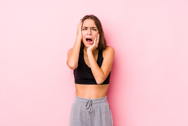 Joven mujer caucásica fitness posando sobre fondo rosa lloriqueando y llorando desconsoladamente.