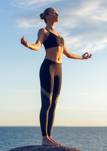 Joven mujer caucásica fitness practicando yoga en la orilla del mar